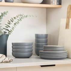 grey bowls and plates sit on a shelf next to a vase with greenery in it