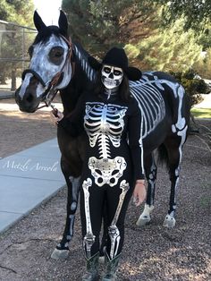 a woman in skeleton makeup standing next to a horse