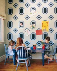 two children sitting at a table in front of a wall with geometric designs on it