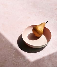 a white plate with a pear on it sitting on a pink table top next to a window