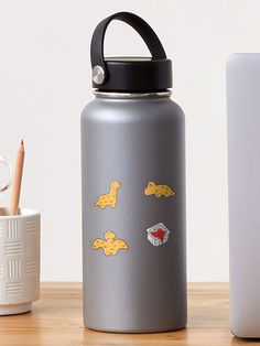 a silver water bottle with yellow stickers on it next to a cup and laptop