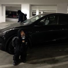 a man standing next to a black car in a parking garage