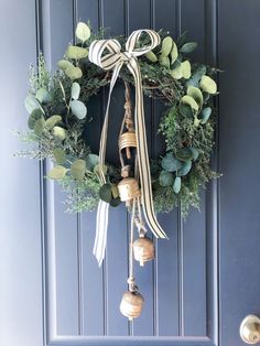 a wreath hanging on the front door with bells and greenery tied to it's sides