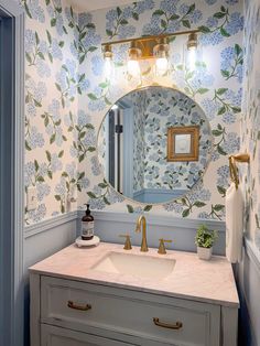 a bathroom with blue and white wallpaper, gold faucet, sink and mirror