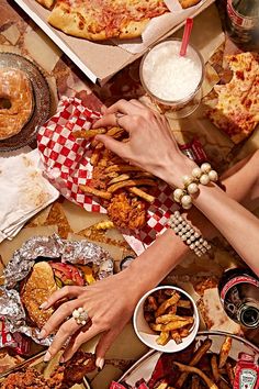 several people are eating pizza and french fries at a table full of different types of food