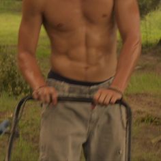 a shirtless man with no shirt holding a metal object in his hand while standing on the grass