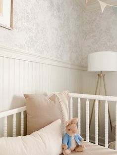 a teddy bear sitting on top of a bed next to pillows and a lamp in a room