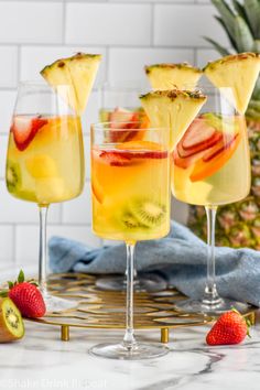 three glasses filled with fruit punch on top of a table next to sliced pineapples