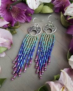 a pair of earrings with beads hanging from it's earring hooks next to purple flowers