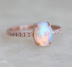 an opal and diamond engagement ring on a white surface with the center stone set in 18k rose gold