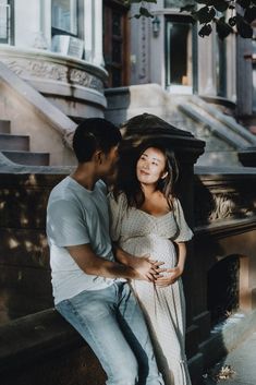 a pregnant woman leaning against a man's back on the steps in front of a building