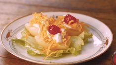 a white plate topped with lettuce covered in cheese and ketchup on top of a wooden table