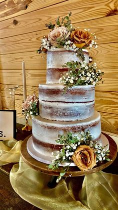 a three tiered cake with flowers and greenery sits on a table next to a sign