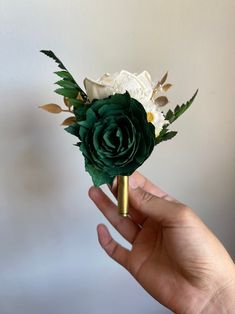 a hand holding a green and white boutonniere