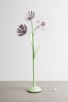 a green vase with three flowers in it on a table next to a white wall