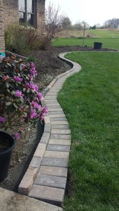 a brick walkway in front of a house with flowers growing on the side and grass around it