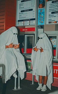 two people in white robes are using their cell phones at a vending kiosk