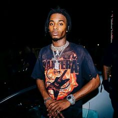 a man standing in front of a car wearing a black shirt and silver bracelets