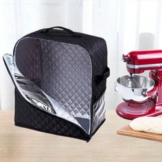 a red mixer sitting on top of a wooden table next to a black and white bag