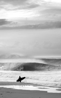 a person carrying a surfboard on top of a sandy beach next to the ocean