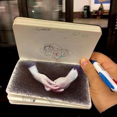 a hand holding an open book with two hands on it and writing on the cover