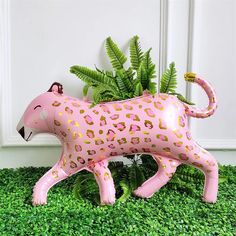 a pink leopard figurine sitting on top of green grass next to a plant