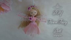 a pink fairy doll hanging from the side of a wall with flowers in front of it