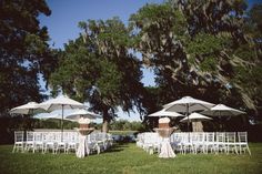 chairs and umbrellas are set up for an outdoor wedding in the grass under trees