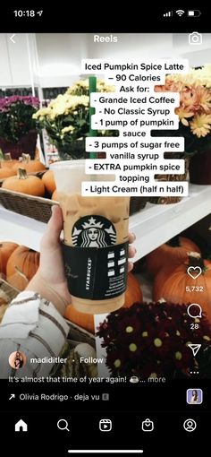 someone holding up a cup of starbucks coffee in front of pumpkins and other flowers