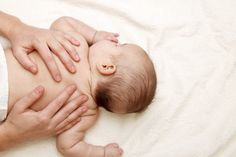 a woman holding a baby on top of a white blanket with her hands around it