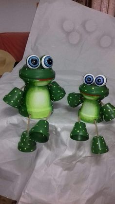 two green frog figurines sitting on top of a white sheet with polka dots