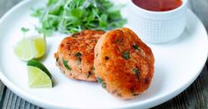 two crab cakes on a white plate with garnishes and lime wedges