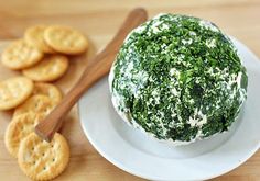 a cheese ball with spinach and crackers on a white plate next to it