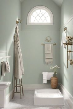 a bathroom with green walls, white fixtures and an arched window in the corner is shown