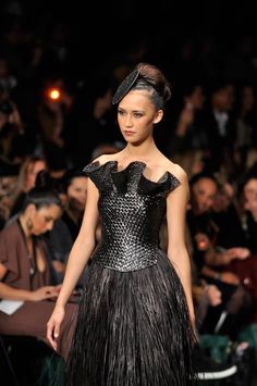 a woman is walking down the runway in a black dress with feathers on her skirt