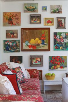 a living room filled with lots of pictures and paintings on the wall next to a couch