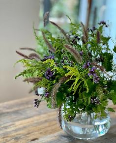 a vase filled with lots of green and purple flowers on top of a wooden table