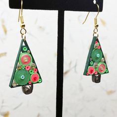 a pair of green and red earrings on a black stand next to a white wall