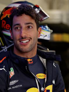 a man wearing a red bull racing suit and holding a helmet on top of his head