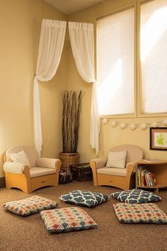 a living room filled with lots of furniture next to two large windows covered in white drapes