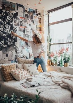 a woman standing on top of a bed in a room with lots of pictures on the wall