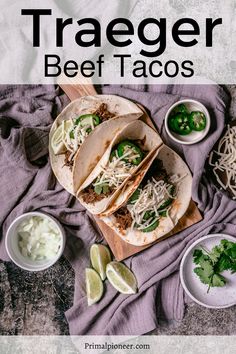 three beef tacos on a cutting board with limes and cilantro