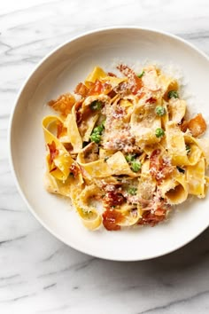 a white bowl filled with pasta and vegetables on top of a marble countertop next to a fork