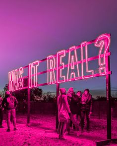 a group of people standing under a neon sign that says what's it really?