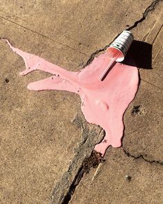 a bottle of pink paint sitting on the side of a road next to a sidewalk