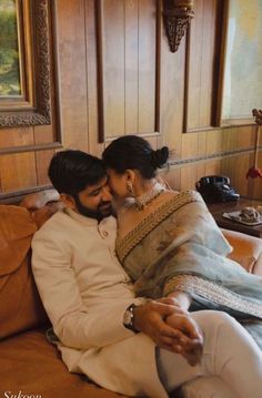 a man and woman sitting on top of a couch in front of a wall with wooden paneling