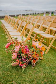 rows of wooden chairs with flowers in them on the grass at an outdoor wedding ceremony