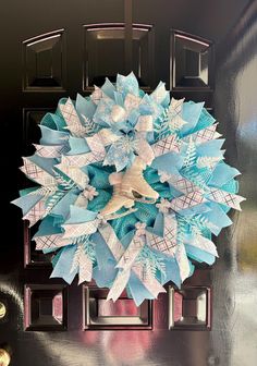 a blue and white paper snowflake wreath on a black front door with gold bells