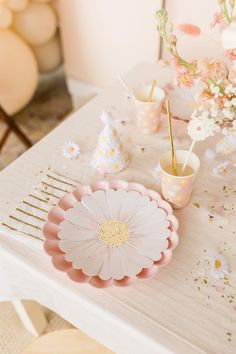 a white table topped with pink plates and cups filled with flowers on top of it