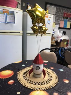 a small rocket ship on top of a table with gold balloons in the shape of stars